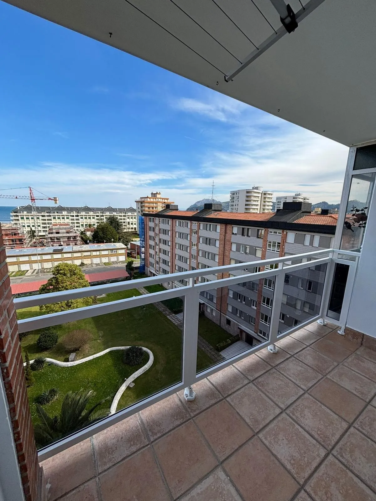 Barandilla de aluminio blanco y vidrio en una terraza alta, con jardín, edificios y el mar al fondo
