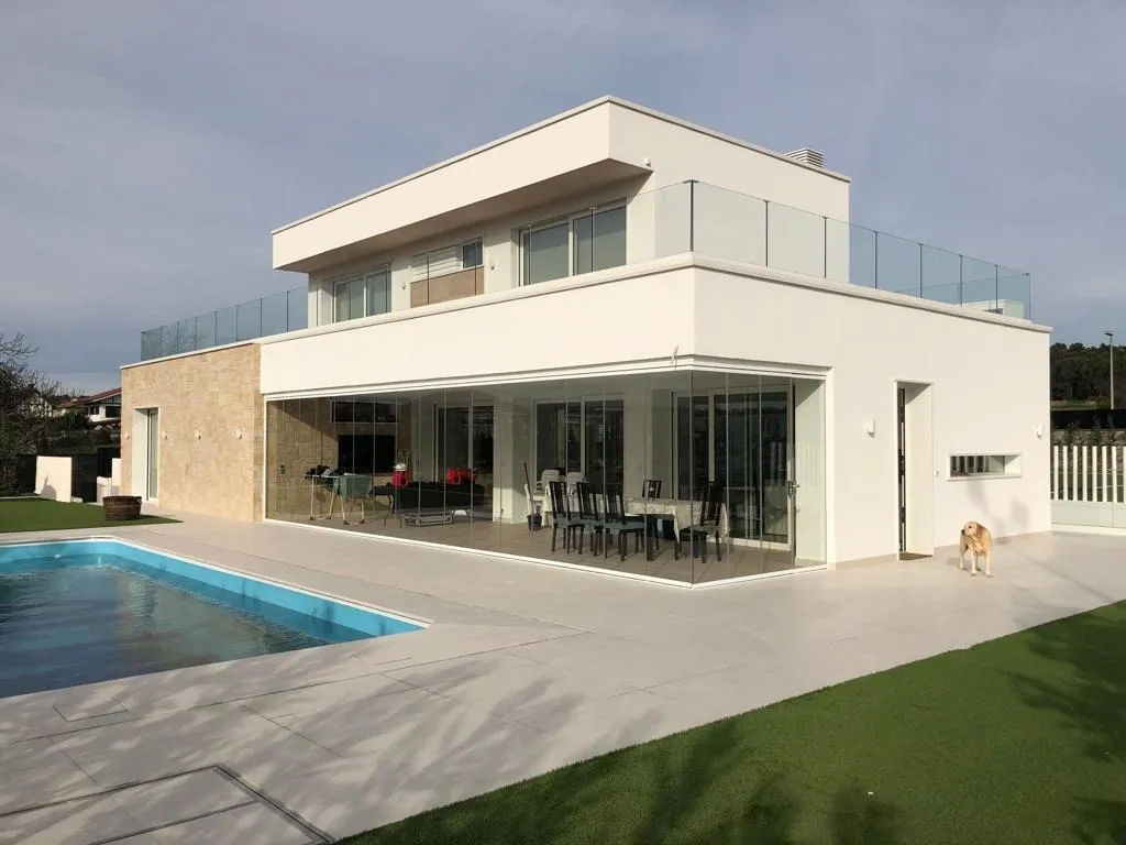 Fachada de un chalet en Vizcaya con porche acristalado y barandillas de vidrio en la terraza superior