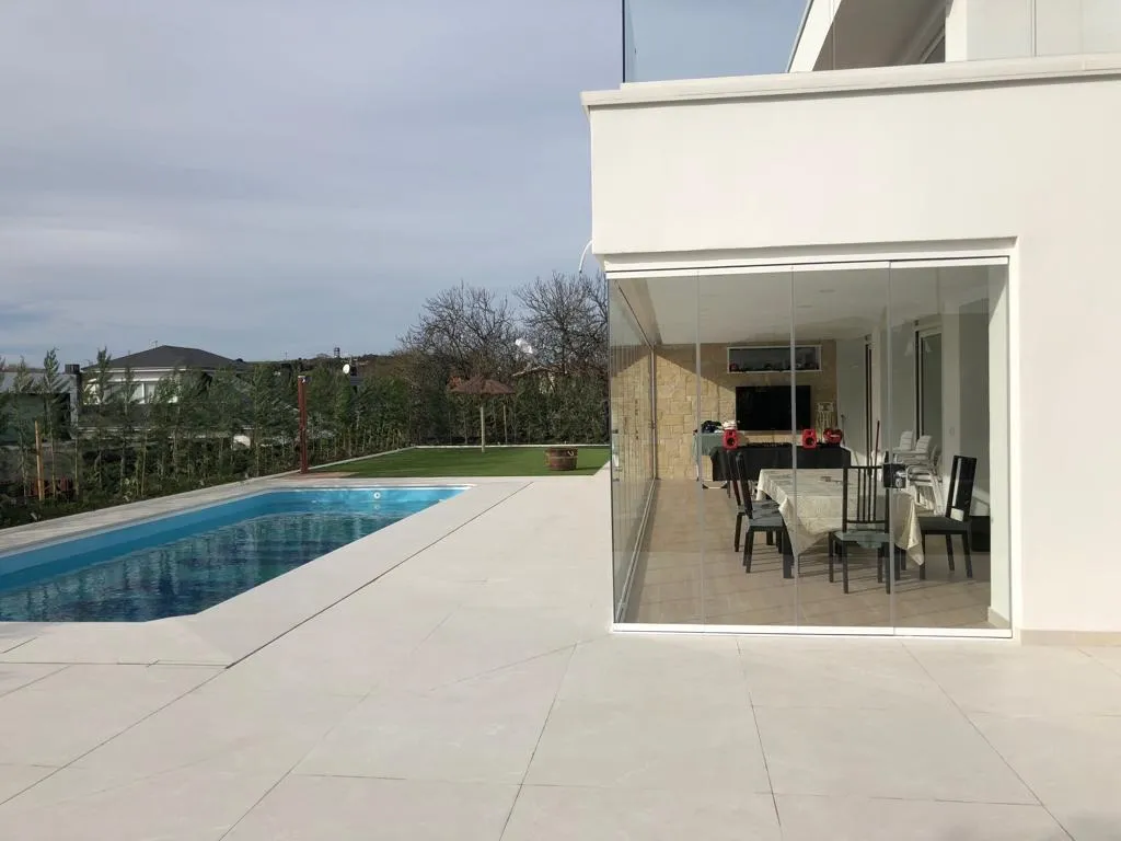 Cierre acristalado de aluminio blanco en el porche, visto desde la piscina