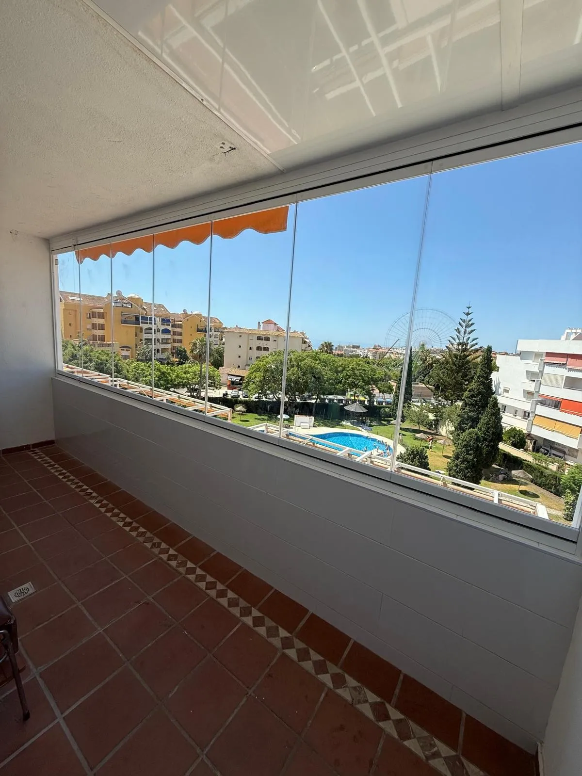 Terraza cerrada con cortina de vidrio, con vistas a una piscina comunitaria y jardines