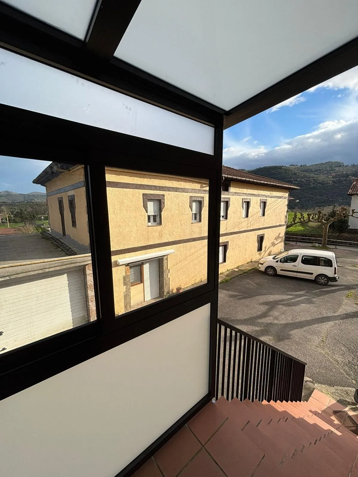 Cerramiento acristalado de aluminio negro con techo translúcido sobre el rellano de una escalera exterior