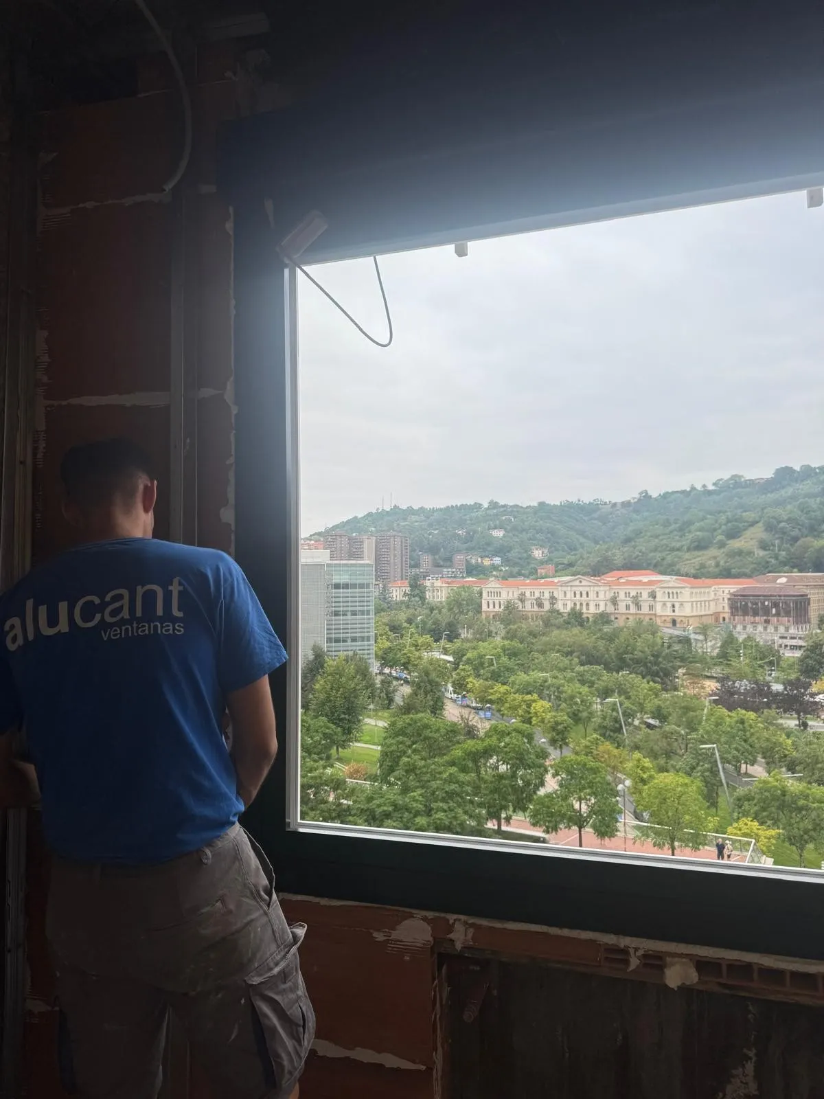 Instalador de Alucant, con la camiseta de la empresa, junto a una ventana recién colocada con vistas a la ciudad