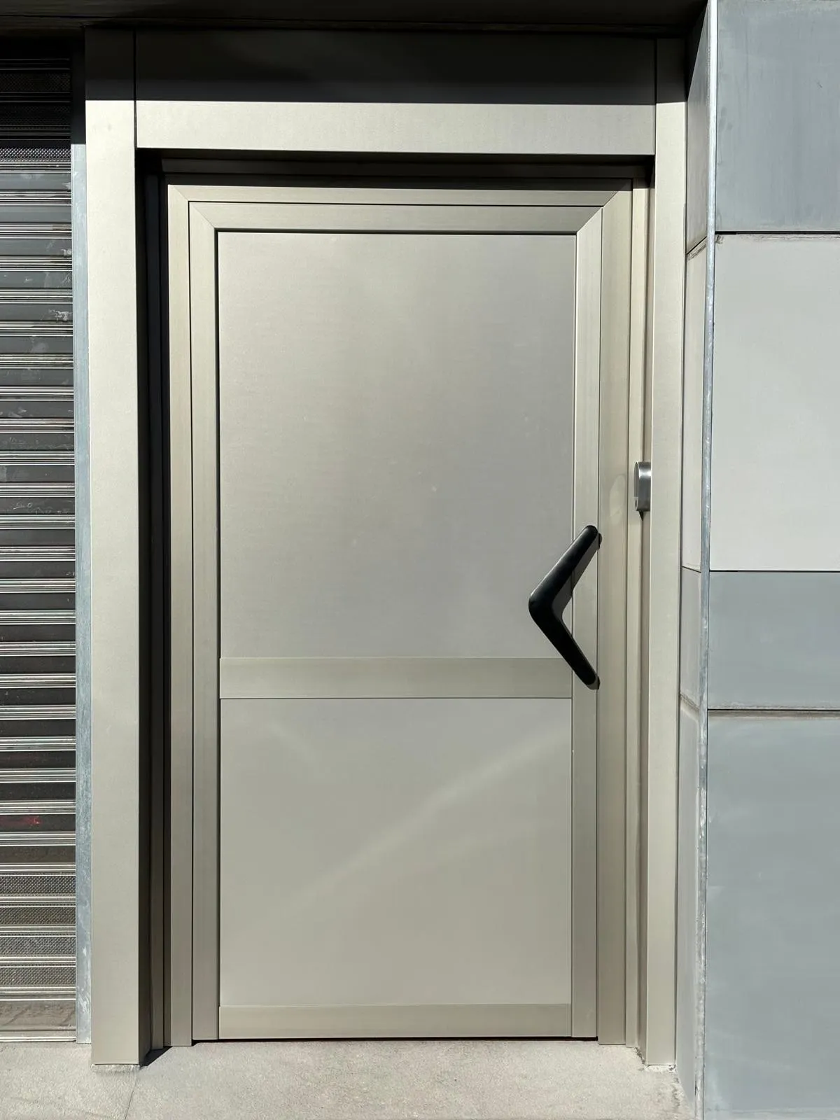 Puerta de aluminio en tono champán con paneles lisos y tirador negro en ángulo