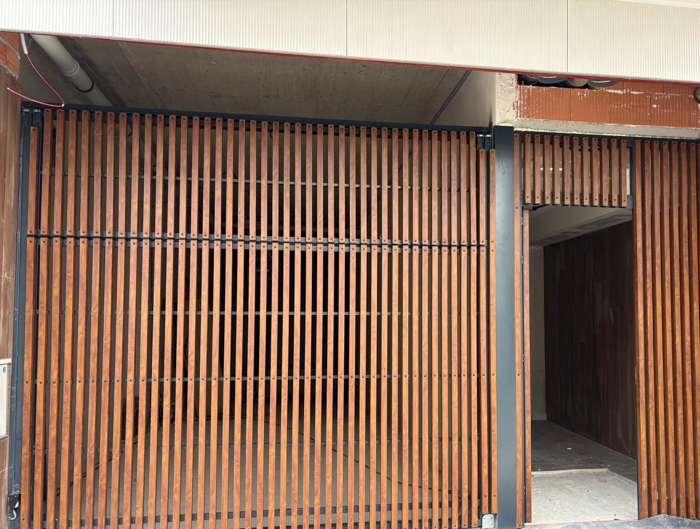 Puerta de garaje y puerta de acceso con lamas verticales en acabado madera sobre estructura oscura