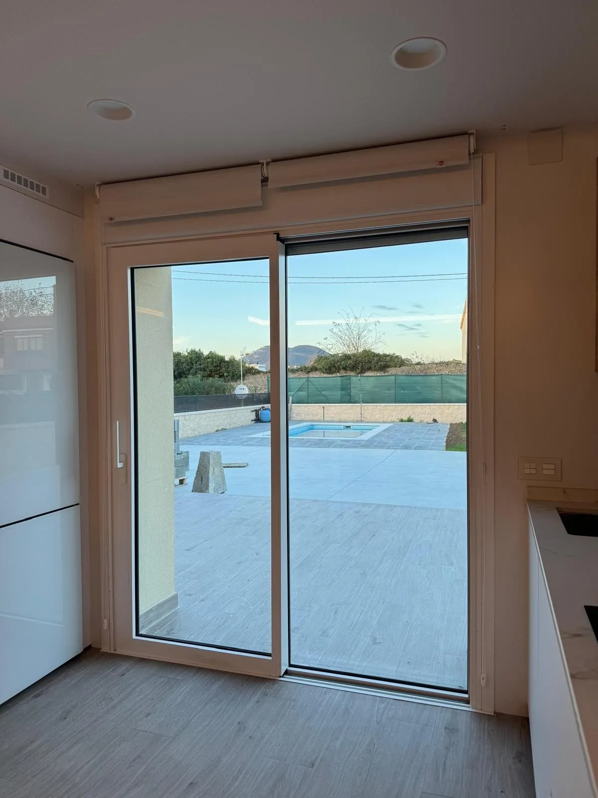 Ventanal corredero en blanco visto desde la cocina, con la terraza y la piscina al otro lado